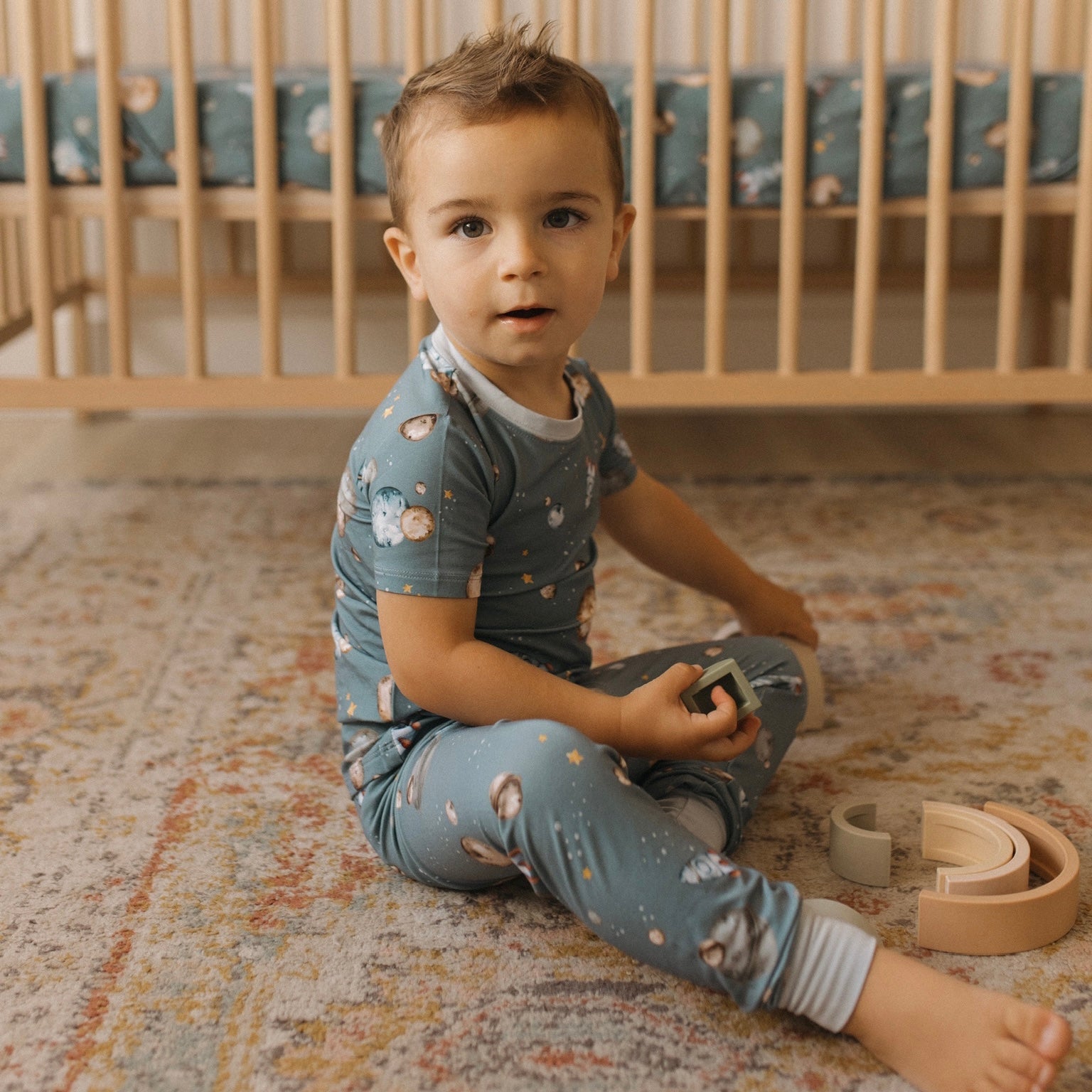 Young child playing with rainbow in space themed bamboo pajamas