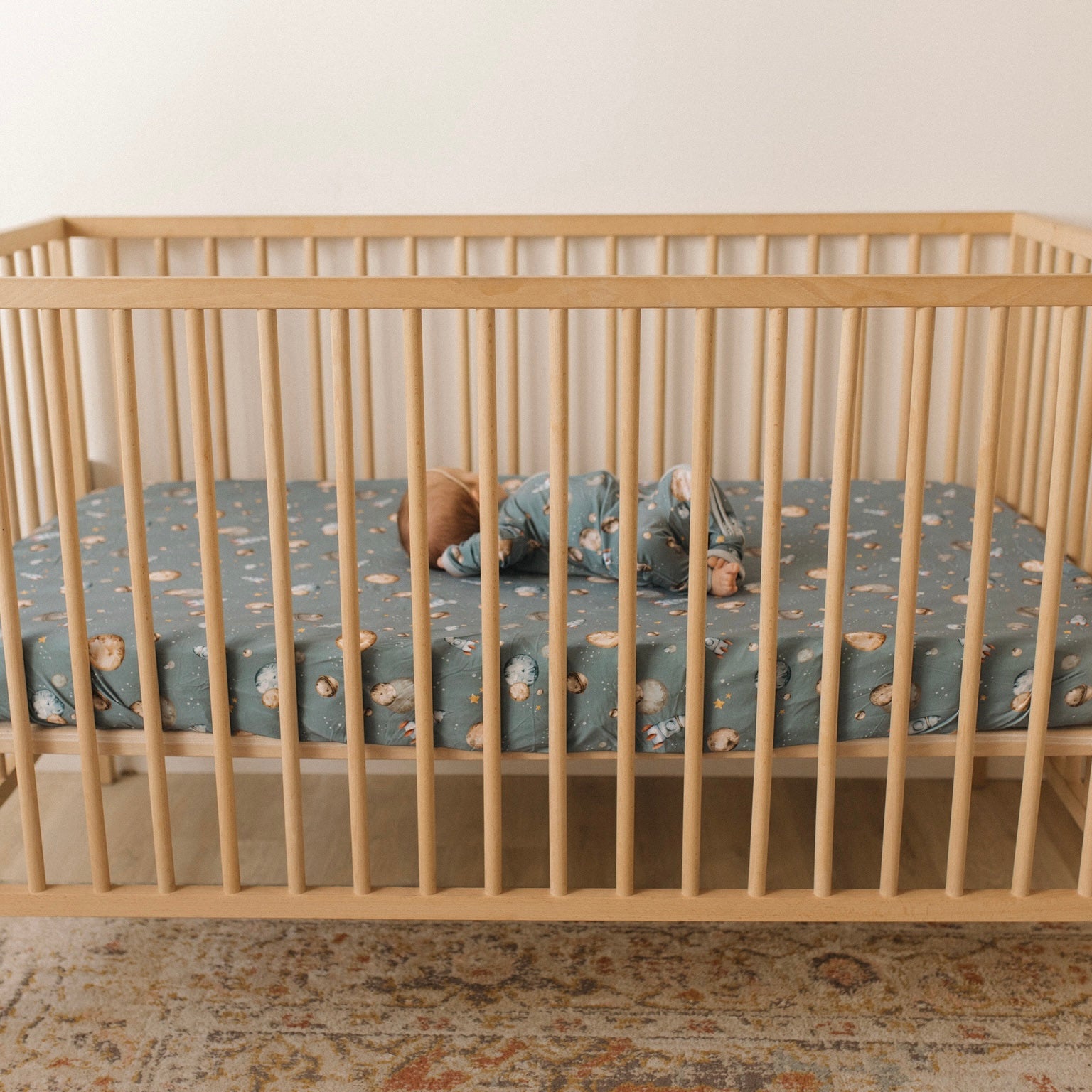 baby laying in a crib, in space themed bamboo pajamas