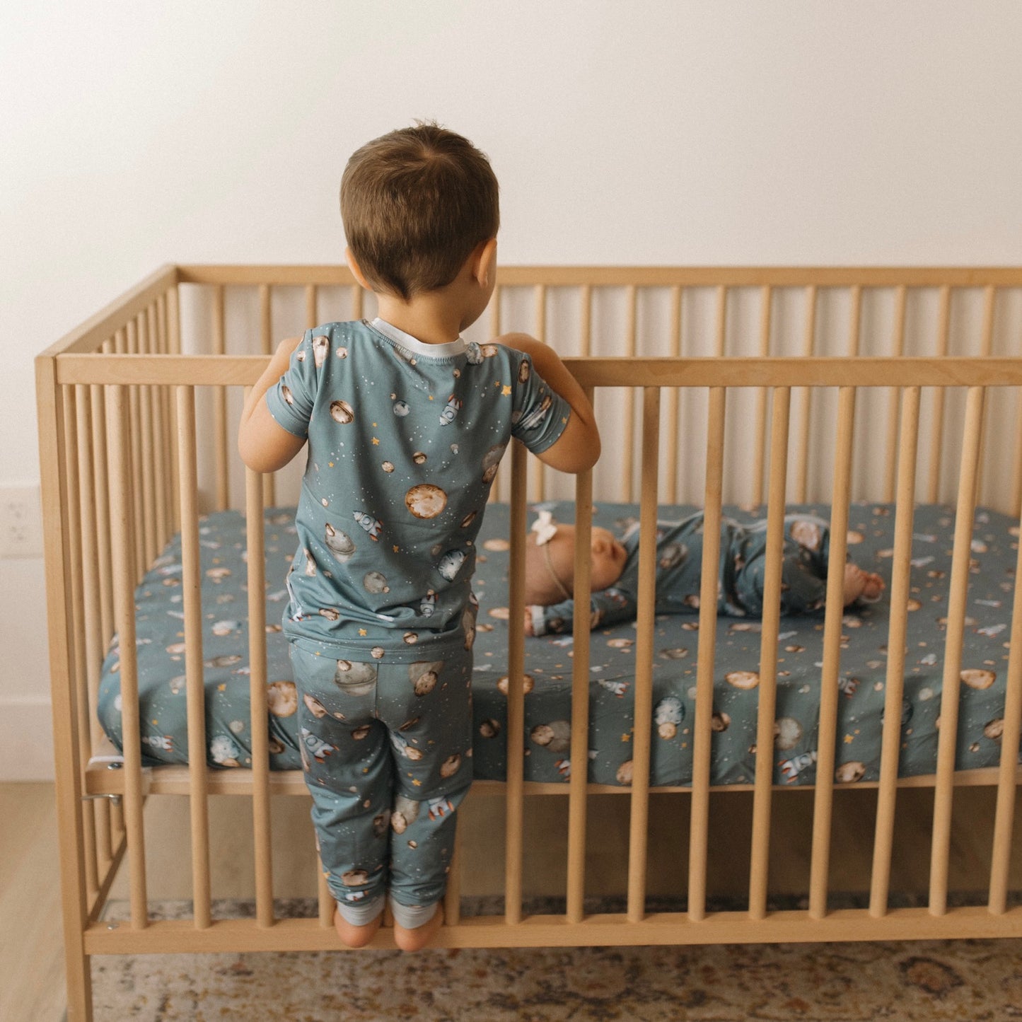 Toddler in space  bamboo pajamas hanging on crib while baby is laying on crib