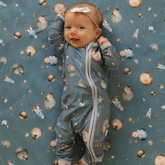 Baby in space themed bamboo pajamas laying down on space themed bamboo crib sheet